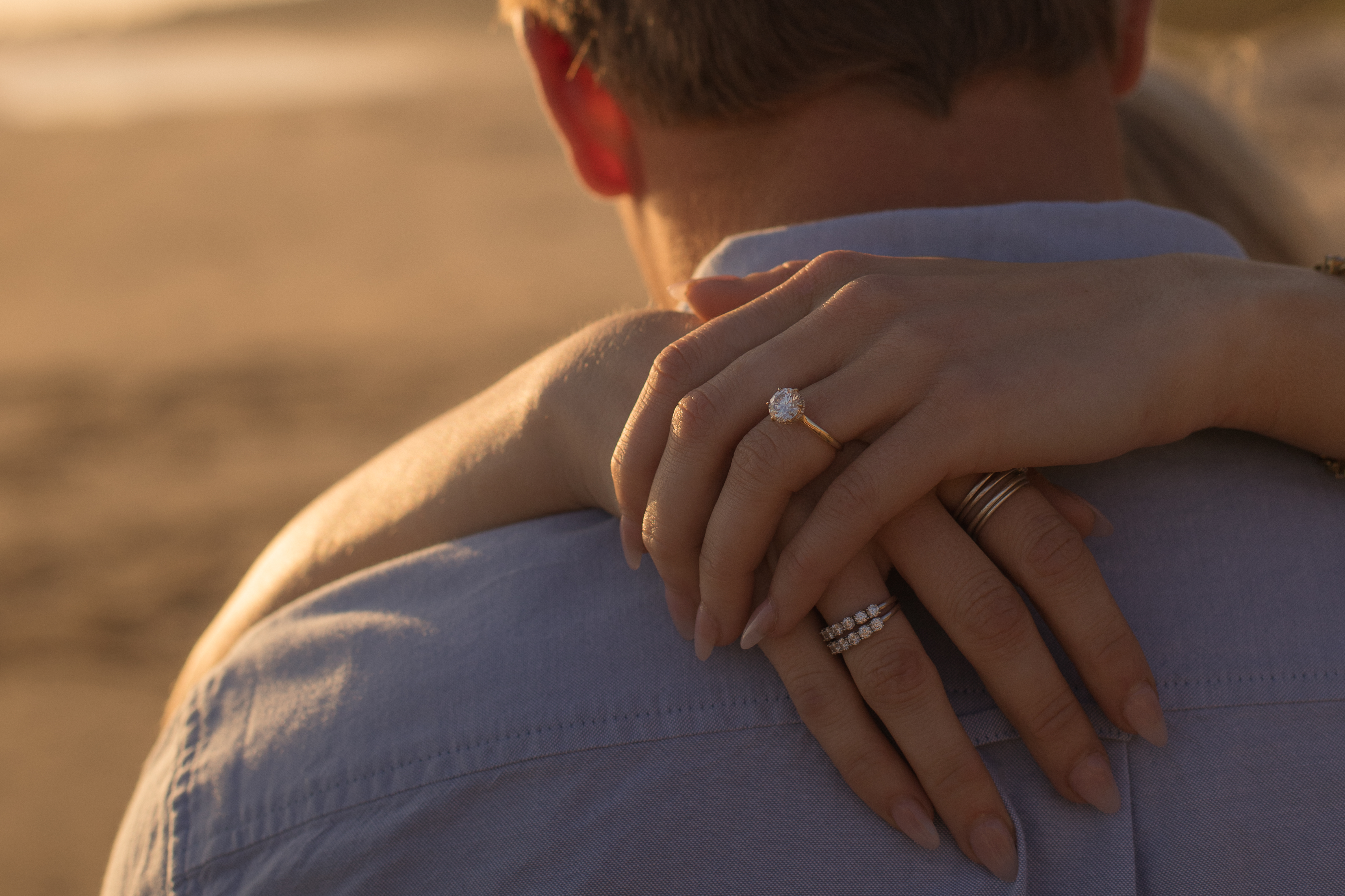 Close-up of a bride's engagement ring as her arm rests on the groom's shoulder at sunset