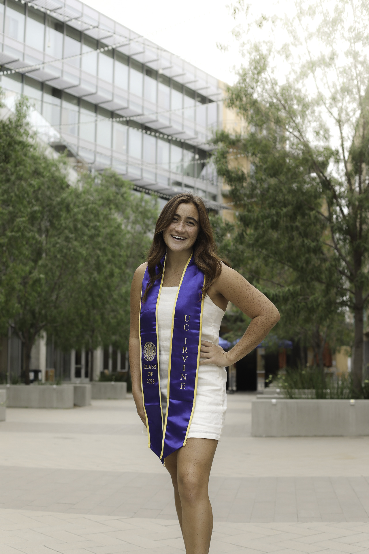 UC Irvine Class of 2023 graduate in a white dress and purple stole on campus
