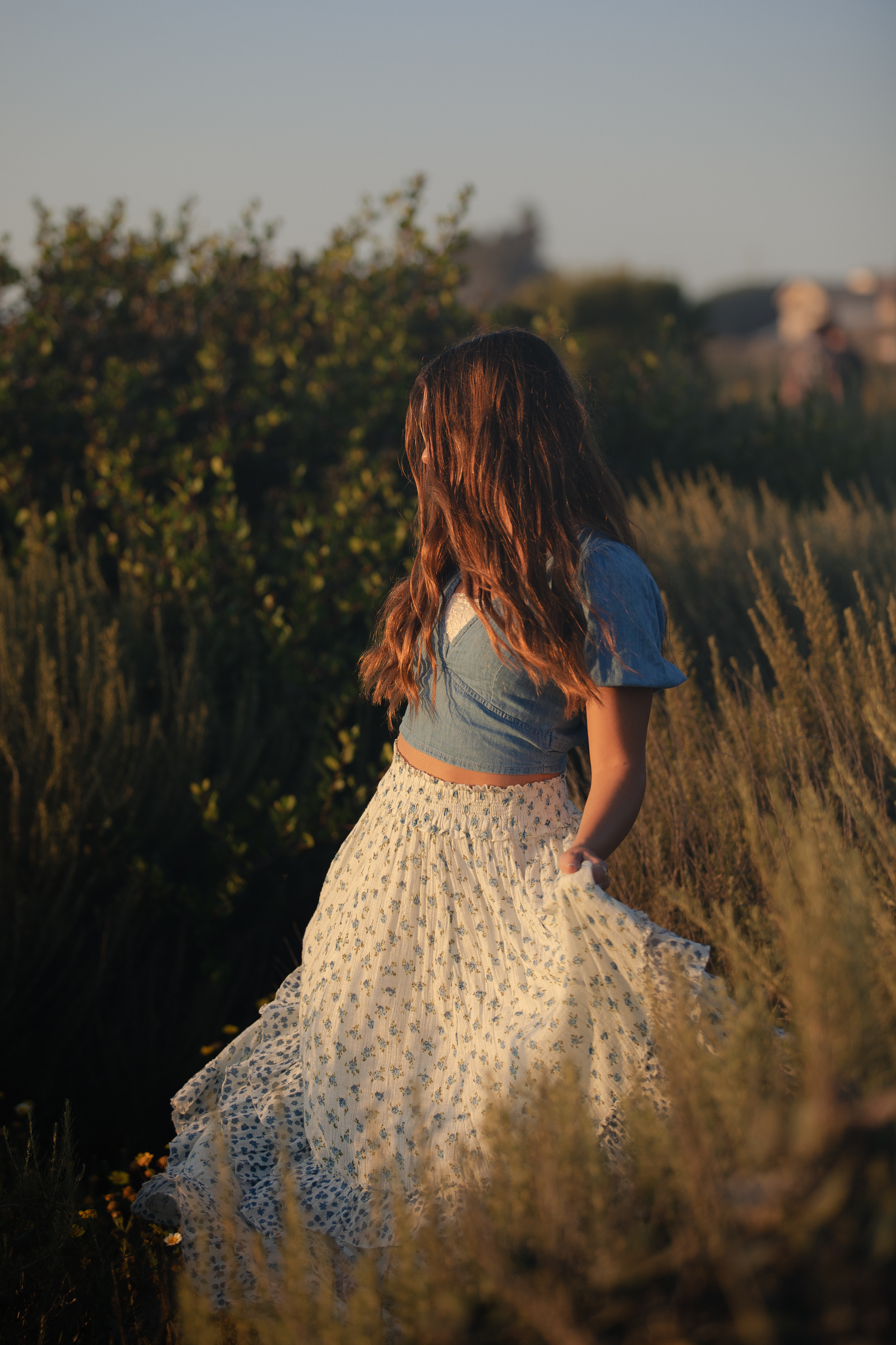 Senior portrait of a girl walking through coastal brush in a floral skirt and denim top